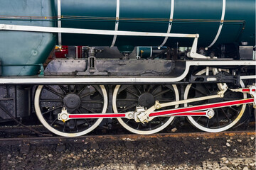 Steam engine train locomotive details of mechanical parts close-up. Old black iron with red accents railway locomotive wheels and rods on rail track. Retro historical transport technology concept.