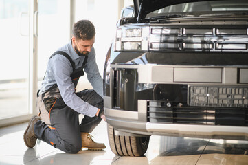Leinwandbilder - Friendly mechanic in modern car repair shop with car. Professional technician checking vehicle diagnostics and maintenance. Concept of automotive industry and customer service