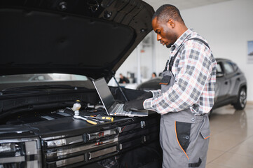 Poster - Portrait of smiling mechanic in car service ordering new parts for damaged vehicle using tablet. African american repairman looking online for components to replace old ones in busted automobile
