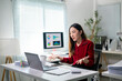 © Apichat - A woman is sitting at a desk with a laptop and a monitor