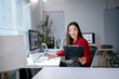 © Apichat - A woman is sitting at a desk with a computer and a clipboard
