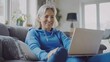 © SebuahKisah - Smiling woman using laptop on couch at home
