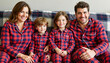 © Nii_Anna - Happy family wearing matching pajamas on a cozy couch, family bonding