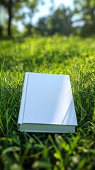 Poster - Pristine White Book on Fresh Green Grass in Natural Sunlight Outdoors : Generative AI