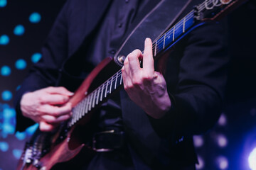 Wall Mural - Concert view of an electric guitar player with vocalist and rock band performing in a club, male musician guitarist on stage with audience in a crowded concert club hall arena, hands on a guitar