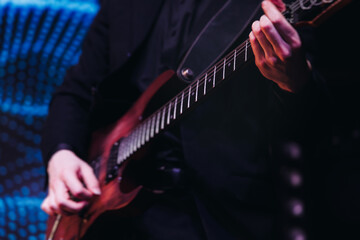 Wall Mural - Concert view of an electric guitar player with vocalist and rock band performing in a club, male musician guitarist on stage with audience in a crowded concert club hall arena, hands on a guitar