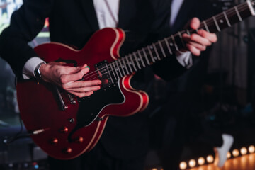 Wall Mural - Concert view of an electric guitar player with vocalist and rock band performing in a club, male musician guitarist on stage with audience in a crowded concert club hall arena, hands on a guitar