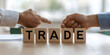 © A2Z AI  - Two hands arranging wooden blocks spelling out the word TRADE.  A concept image representing business deals, agreements, and commerce.