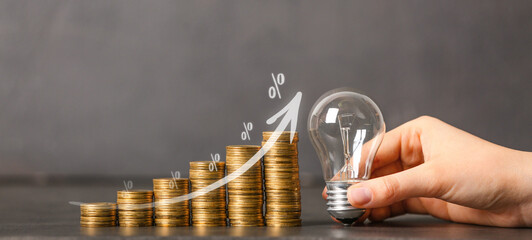 Wall Mural - Female hand with light bulb and coins on grey background. Concept of savings money