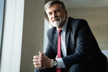 positive successful mature businessman sitting in armchair in modern office
