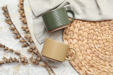 Wall Mural - Different ceramic mugs with dried flowers and wicker mat on light grunge background