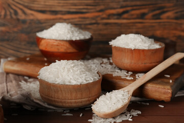 Wall Mural - Spoon and bowls of raw rice on table against wooden background. Closeup