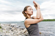 © muse studio - Woman practicing yoga by the lakeshore during a cloudy day with serene water in the background