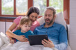 © SpaceOak - Family enjoying a cozy morning together while watching a tablet in bed