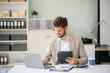 © laddawan - Confident businessman working on finance analysis with a tablet and laptop at office desk.