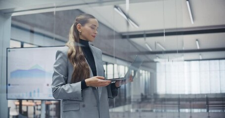 Aufkleber - Elegant Caucasian Woman Standing Next to a Glass Wall in Office, Checking Emails and Scheduling Appointments on Laptop Computer. Manager Maintaining a Busy Schedule in a Professional Environment