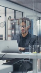 Poster - Vertical Screen: Portrait of a Manager Reviewing Sales Reports on Laptop Computer. Young Man Browsing Data to Identify Key Trends and Opportunities in a Modern Office Workspace with Diverse Employees