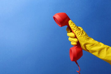 Wall Mural - Woman in rubber glove holding red telephone handset on blue background, closeup. Space for text