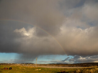 Fototapete - Cloudy sky with rainbow and rain over a country side with fields and fences. Irish landscape. Wet weather.