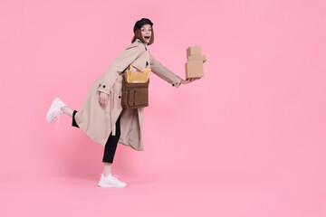 Poster - Happy postwoman with bag and parcels on pink background. Space for text