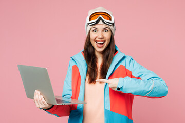 Poster - Skier young IT woman in blue padded jacket ski goggles mask spend extreme weekend winter season in mountains hold use work point on laptop pc computer isolated on plain pink background Hobby concept