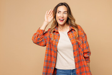 Wall Mural - Young curious nosy smiling woman she wears orange shirt casual clothes try to hear you overhear listening intently isolated on plain pastel light beige background studio portrait. Lifestyle concept.