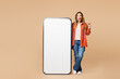 © ViDi Studio - Full body young woman she wear orange shirt casual clothes big huge blank screen mobile cell phone smartphone with workspace copy space mockup area point finger up isolated on plain beige background.