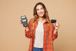 © ViDi Studio - Young woman she wears orange shirt casual clothes hold wireless modern bank payment terminal to process acquire credit card isolated on plain pastel light beige background studio. Lifestyle concept.