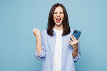 Wall Mural - Young happy Caucasian woman she wears shirt casual clothes hold in hand use mobile cell phone do winner gesture isolated on plain pastel light blue cyan background studio portrait. Lifestyle concept.