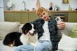 © LIGHTFIELD STUDIOS - Young man captures a playful selfie with his adorable Australian Shepherd in a stylish home.