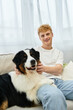 © LIGHTFIELD STUDIOS - A young man with red hair relaxes at home, joyfully playing with his adorable dog.
