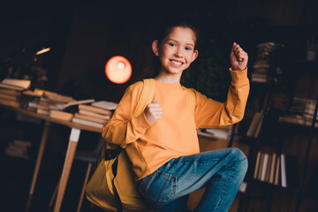 Smiling young girl celebrates achievements while posing indoors with vibrant home background and casual attire