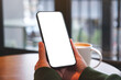 © Farknot Architect - Mockup image of a woman holding mobile phone with blank desktop screen in cafe