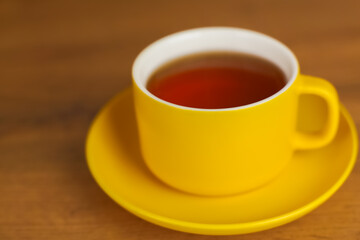 Wall Mural - A mug with a yellow saucer stands on a wooden table, fragrant black tea is poured into it. High quality photo