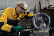 © amorn - Factory woman worker at work in the industry factory, work with CNC machine. Factory female worker maintaining machine in the industrial factory. Female engineer checking parts of lathe machine