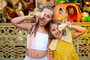 children in the amusement park and attractions, happy children eating ice cream and enjoying the holidays and summer, two girls came to the carousel