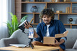 © Liubomir - Man writes negative review about product purchased in online store. Influencer blogger sits at home on sofa in living room, uses tripod and phone to record online video stream.