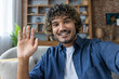 © Liubomir - A man looks into the phone camera, happily waves his hand, takes a selfie photo and talks to colleagues and friends remotely using a smartphone app for video chats.