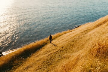 Wall Mural - a person stands at the top of a hill overlooking a calm body of water, ideal for scenic photography 