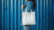 © Fenny - Woman holding blank tote bag, blue wall background, mockup