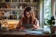 © Vitalii Shkurko - A woman sits at a kitchen table, focused on her tablet as she organizes her finances. Soft evening light creates a warm atmosphere, complemented by plants and kitchen decor