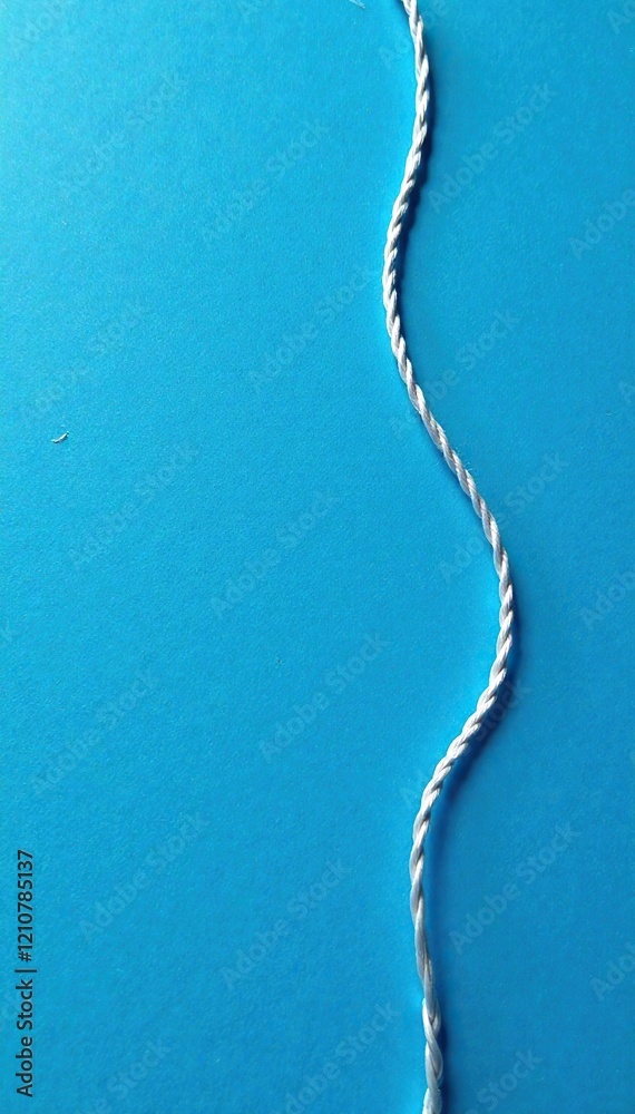 Blue background with a single white thread unwinding from a silver ...