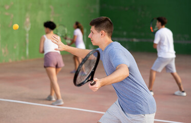 Wall Mural - Young male sportsman preparing to hit ball with racket. Frontenis game on outdoor court