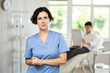 © JackF - Young lady wearing medical scrub standing at treatment room in front of male patient lying at examination couch