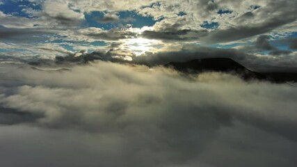 Wall Mural - flying between the clouds. aerial view of clouds, sun, and mountains at sunrise. traveling by air ba
