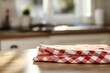 © BerkahStock - Red checkered kitchen towels folded on a wooden table in a sunlit kitchen.