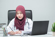 © maya1313 - The Asian Muslim woman doctor was sitting at the patient's examination table and was examining and talking about the patient with a smiling and worried face at hospital.