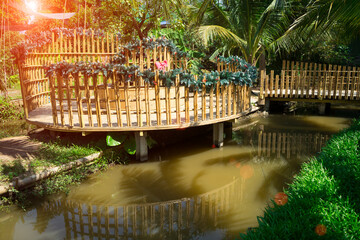 Wooden terrace  with bamboo bridge to reach in the canal at the park  with tree and sunlight background at the garden house.