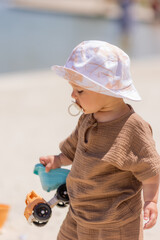 Wall Mural - toddler boy plays on a sandy beach in a panama hat and cotton clothes in summer