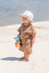 Wall Mural - toddler boy plays on a sandy beach in a panama hat and cotton clothes in summer